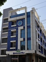 Un edificio de hotel de varios pisos con diseño moderno, que presenta un llamativo ventanal circular en el segundo piso y un letrero que dice "Hotel Continental Blue".