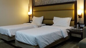 A hotel room with two single beds, a nightstand with a lamp, and an air conditioning unit on the wall.