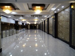 A long, well-lit corridor with reflective flooring, decorative ceiling lights, and patterned wall panels.