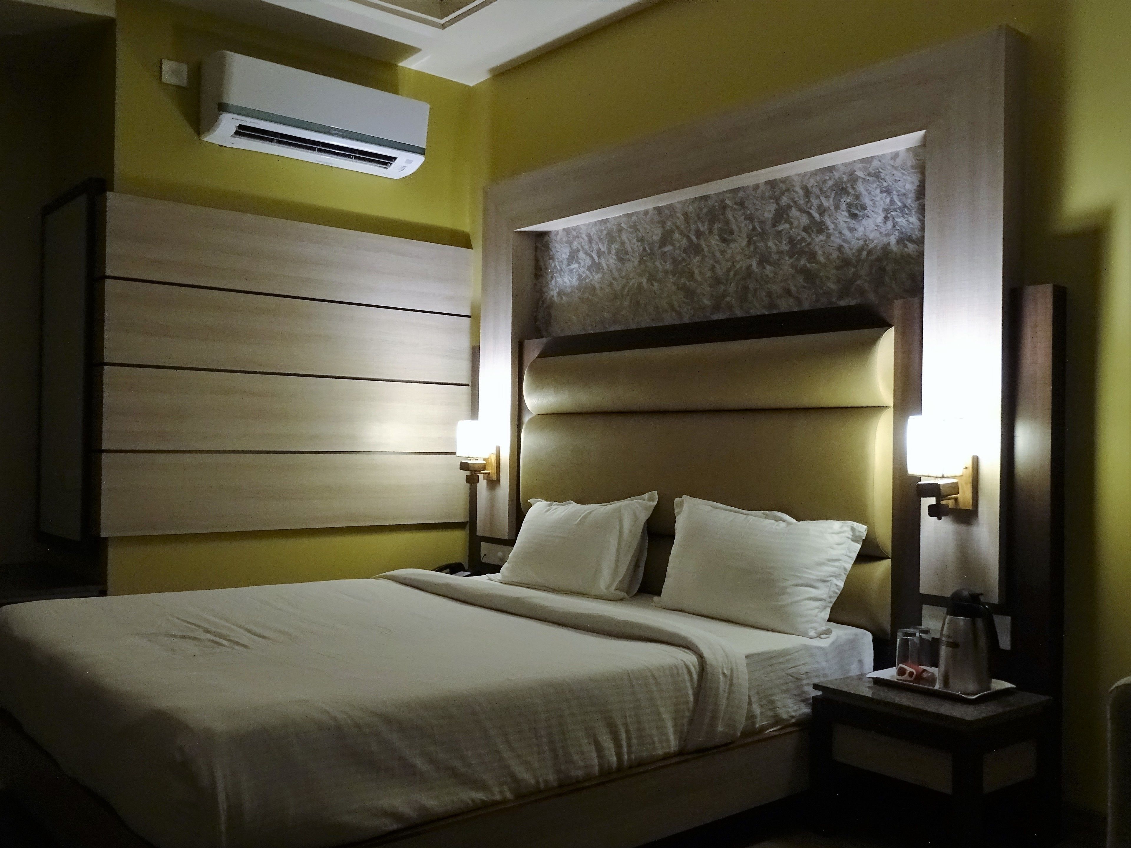A hotel room with a large bed, a headboard with a textured design, and a wall-mounted air conditioner.