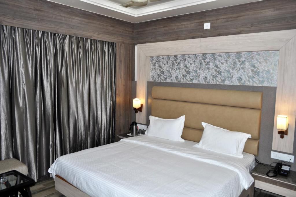 Ein Hotelzimmer mit einem großen Bett, einem Nachttisch, einer Lampe und einem Vorhang.