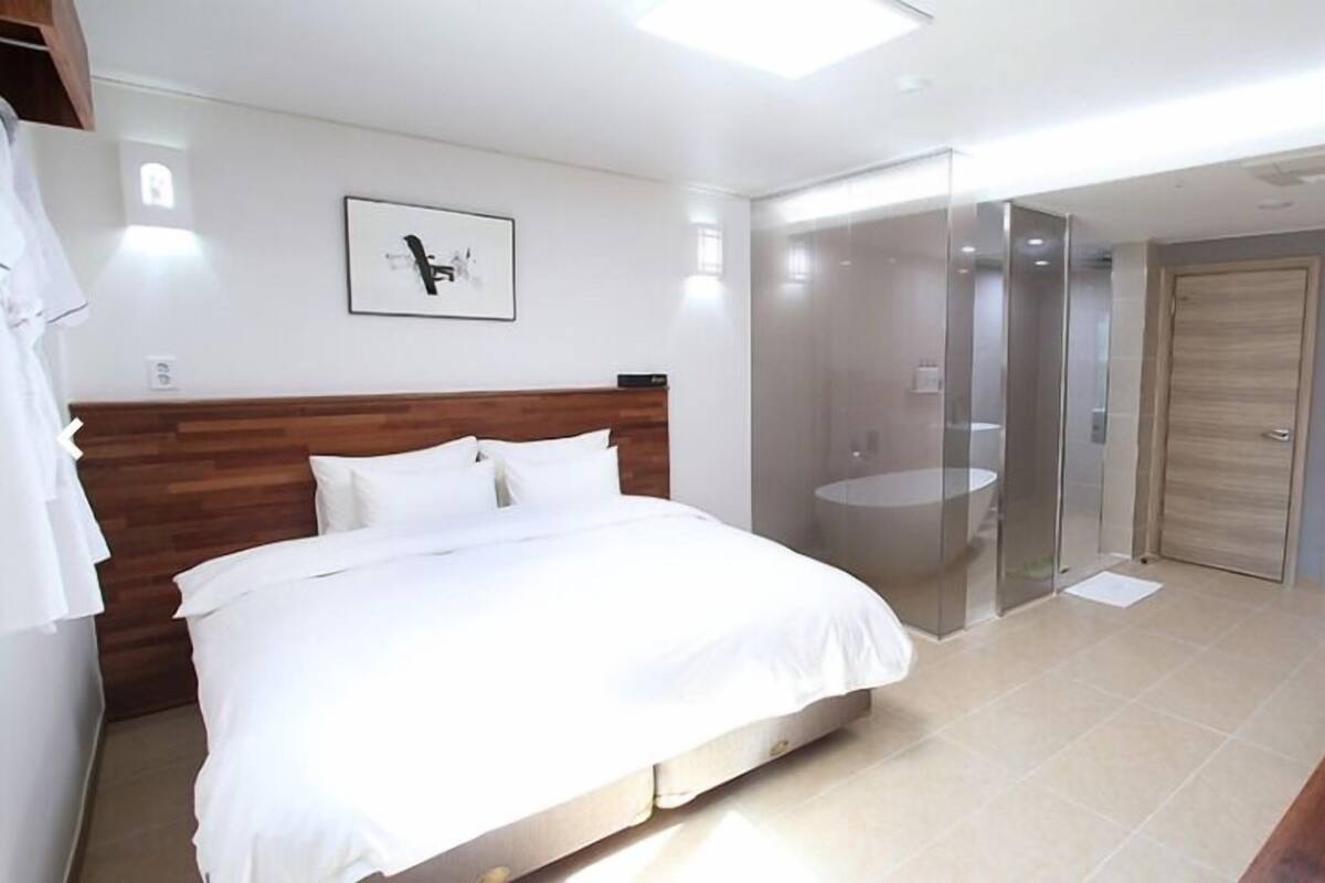 Un dormitorio moderno con una cama de cabecera de madera, ducha con cerramiento de vidrio y armario de madera.