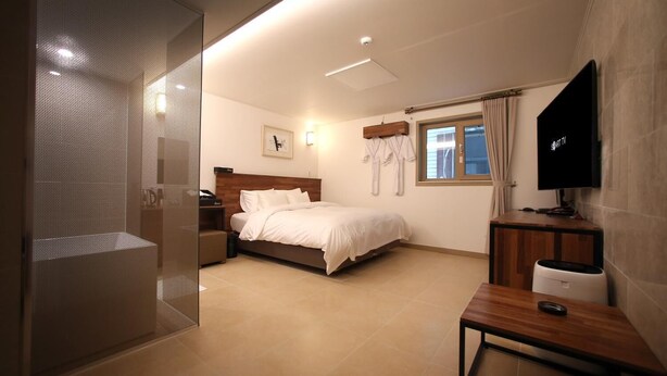 A hotel room with a bed, bedside table, TV, and a shower area. - Hotel You&I (Incheon)