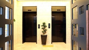A modern elevator area with two elevators, a potted plant, and a tactile paving strip. - Hotel You&I (Incheon)