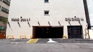 A modern hotel entrance with a flat facade, a clear sky, and a parking area with yellow barriers. - Hotel You&I (Incheon)