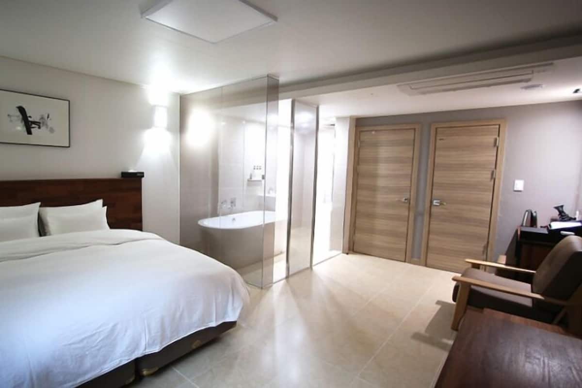 Una habitación de hotel con una cama grande, un baño con bañera y un escritorio con silla.