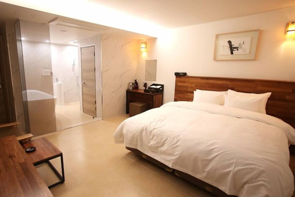 Habitación de hotel con cama, escritorio, mesita de noche, espejo y puerta que da a un baño.