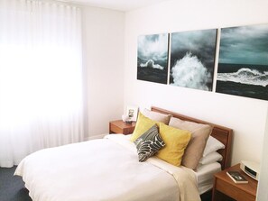 Relax in a serene space with a comfortable bed, a nightstand, and a beautiful ocean-inspired artwork.