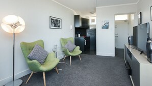 Un salon moderne avec deux fauteuils verts, une petite table ronde, un lampadaire et un téléviseur à écran plat.
