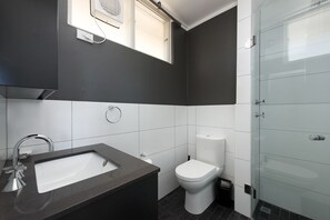 Ein modernes Badezimmer mit dunkelgrauen und weißen Farbtönen, einem Waschbecken mit Armatur, einer Toilette und einer Glasdusche.