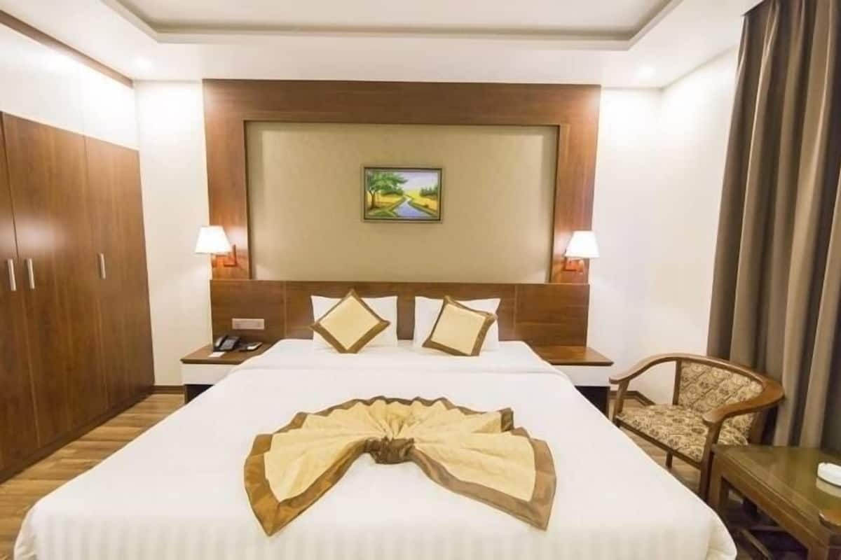 A hotel room with a large bed, two bedside tables with lamps, a wooden headboard with a painting, and a chair.