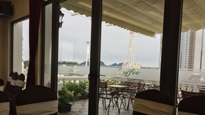 A restaurant with a view of a bridge and a ship. Tables are set with chairs, and there are potted plants on the terrace. - Halong Diamond Hotel (Bai Chay)