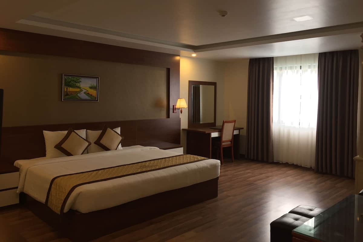 A hotel room with a large bed, a desk with a chair, a mirror, and a painting on the wall.