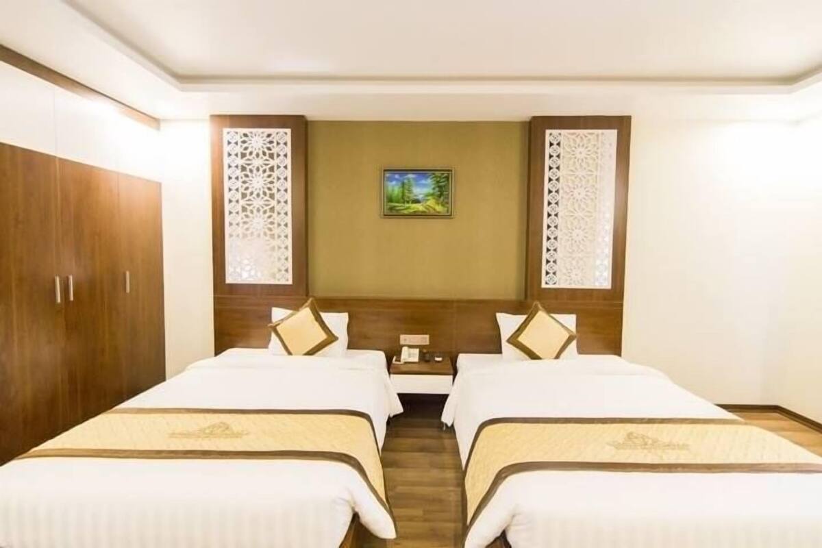 A hotel room with two beds, a wooden wardrobe, decorative panels, and a painting on the wall.
