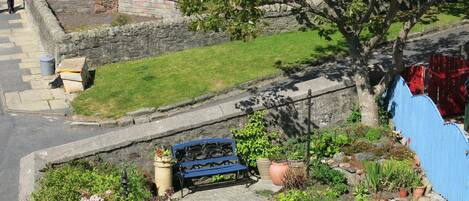 A residential garden with a stone wall, a blue bench, and potted plants.