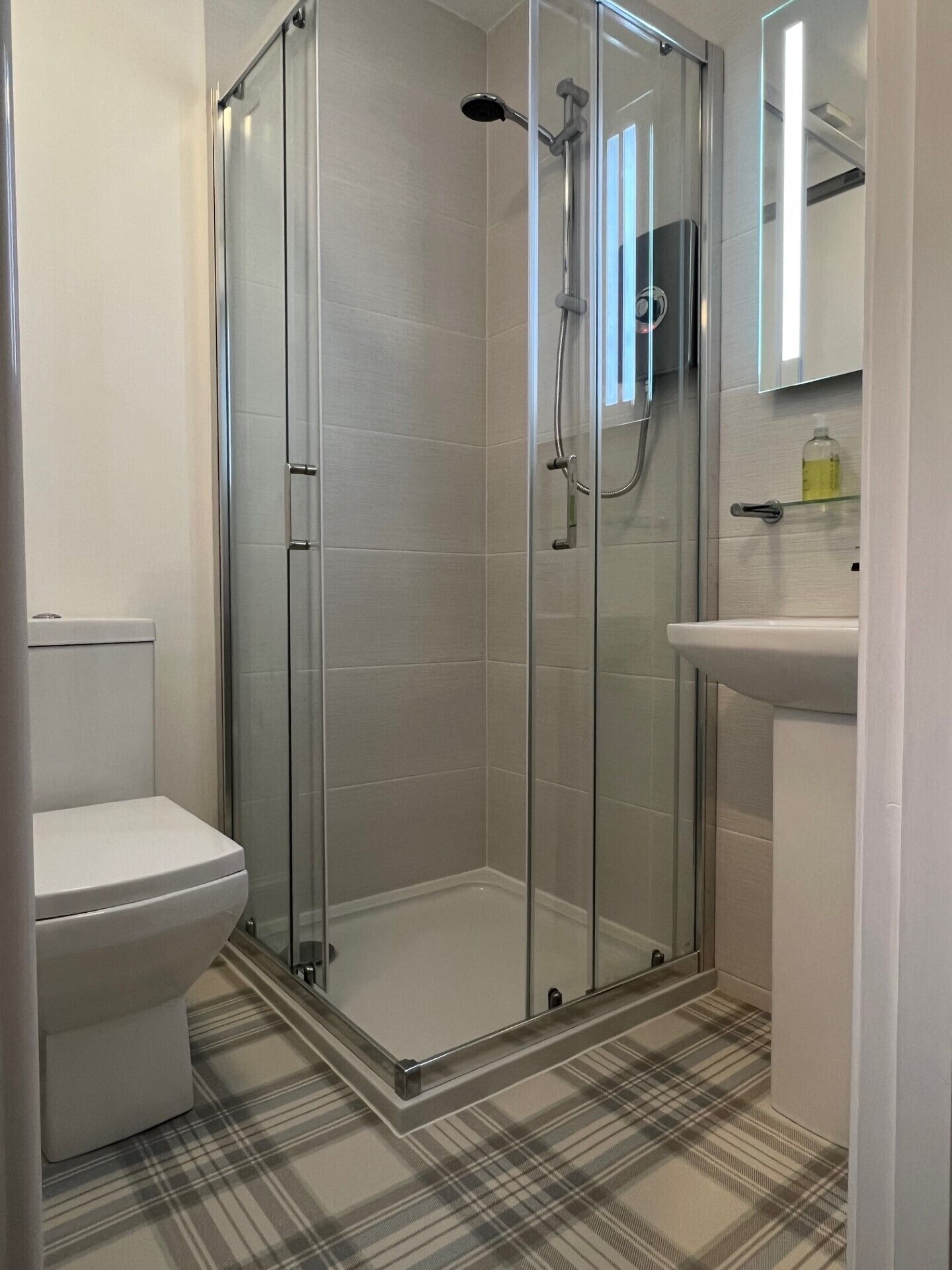 A modern bathroom with a glass-enclosed shower, a white toilet, and a sink with a mirror above it.