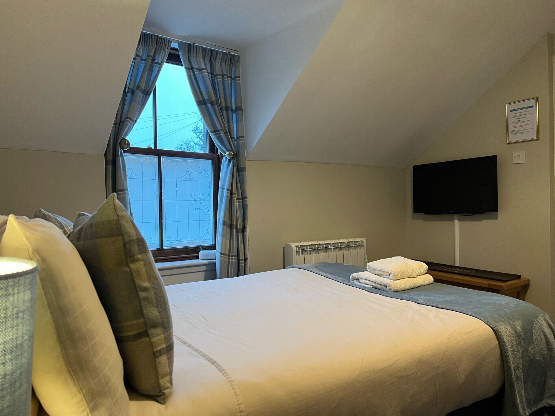 Une chambre d’hôtel avec un grand lit, un téléviseur à écran plat fixé au mur et une fenêtre avec des rideaux.