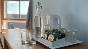 A wooden desk with a bottle of water, a coffee maker, two glasses, and a tray with coffee pods and a mug. - Fort Charlotte Guesthouse (Lerwick)