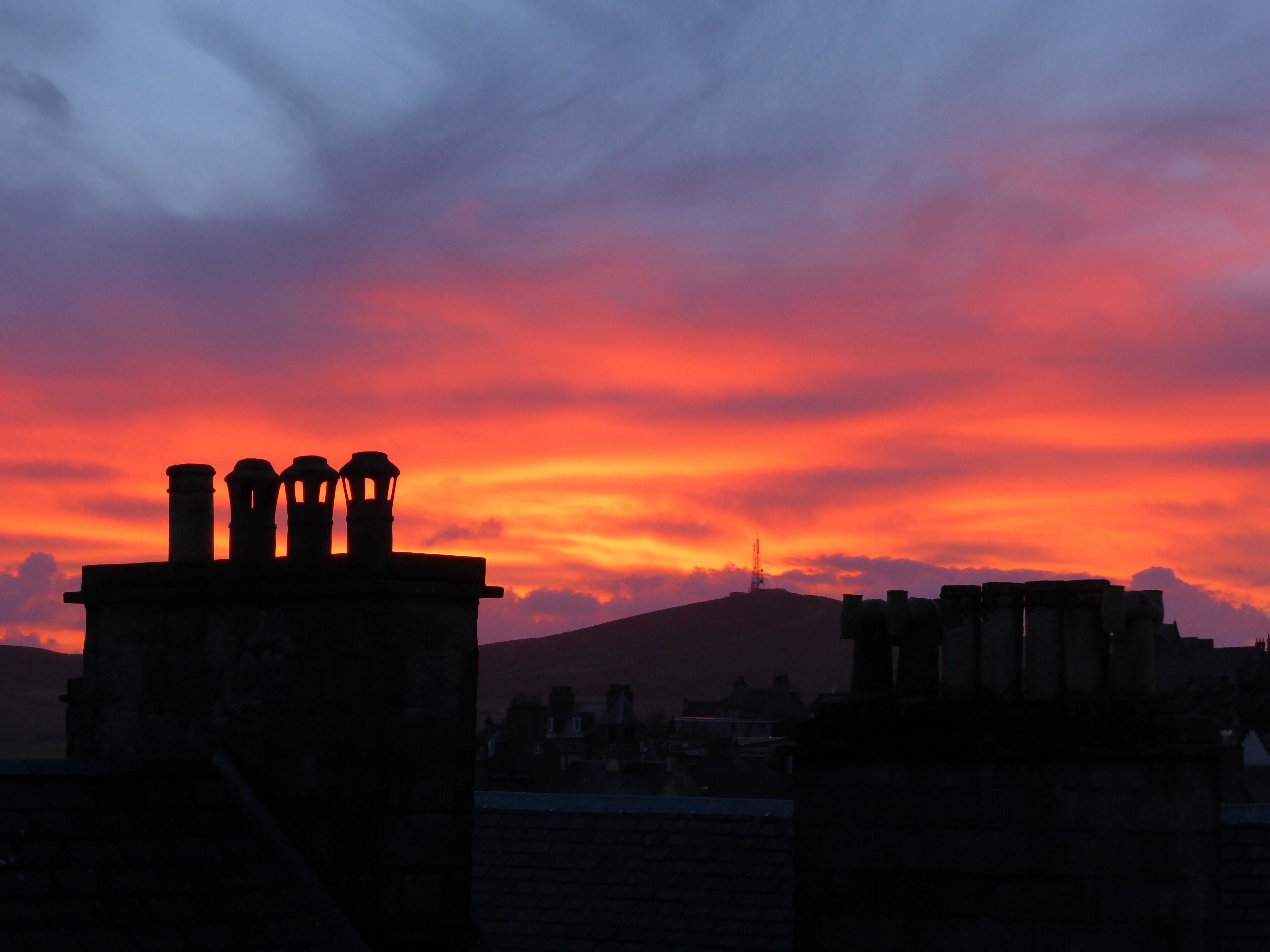 A sunset with a silhouette of a building with three chimneys.