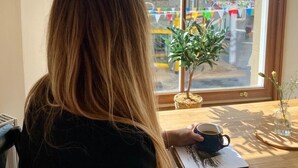 A person seated at a table with a window view of a street and buildings, a small plant, and a cup. - Fort Charlotte Guesthouse (Lerwick)