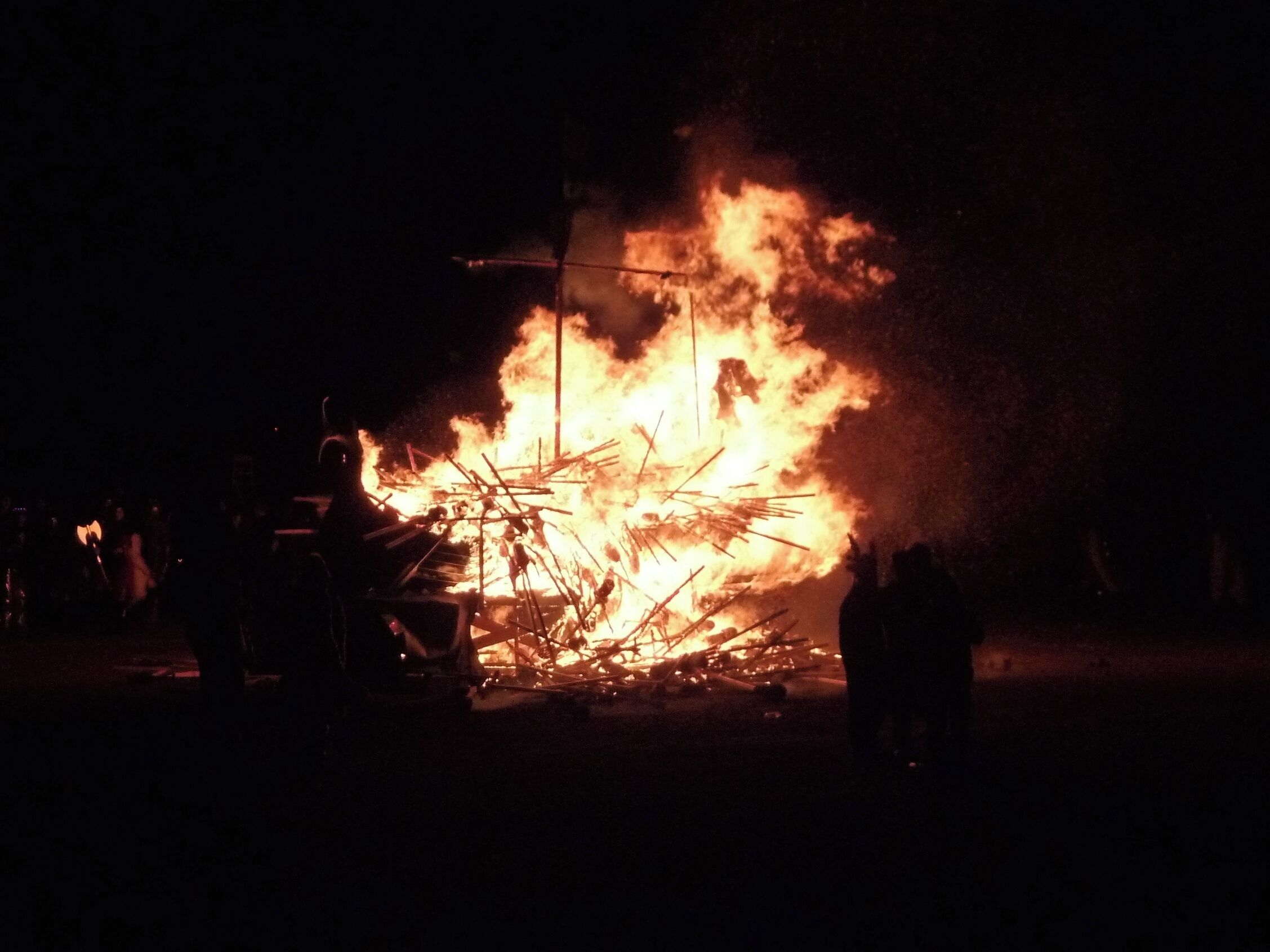 A large fire with flames and smoke, surrounded by people and objects.