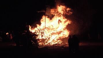 A large fire with flames and smoke, surrounded by people and objects.