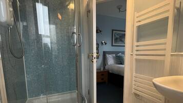 A modern bathroom with a glass-enclosed shower, a white sink, and a visible bedroom in the background.