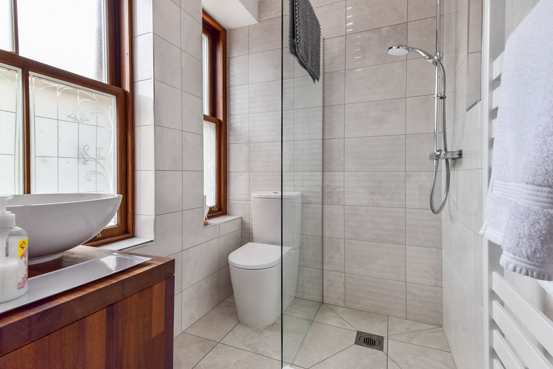 A modern bathroom with a glass shower enclosure, a white sink with a wooden vanity, and a toilet. - Fort Charlotte Guesthouse (Lerwick)