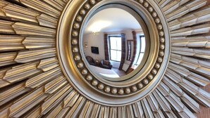 A mirror with a sunburst frame reflecting a room with a sofa, a television, and windows. - Fort Charlotte Guesthouse (Lerwick)