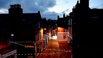 Una calle al anochecer con edificios a ambos lados, una tienda con el rótulo 'INTERSPORT' y luces colgantes a lo largo de la acera.