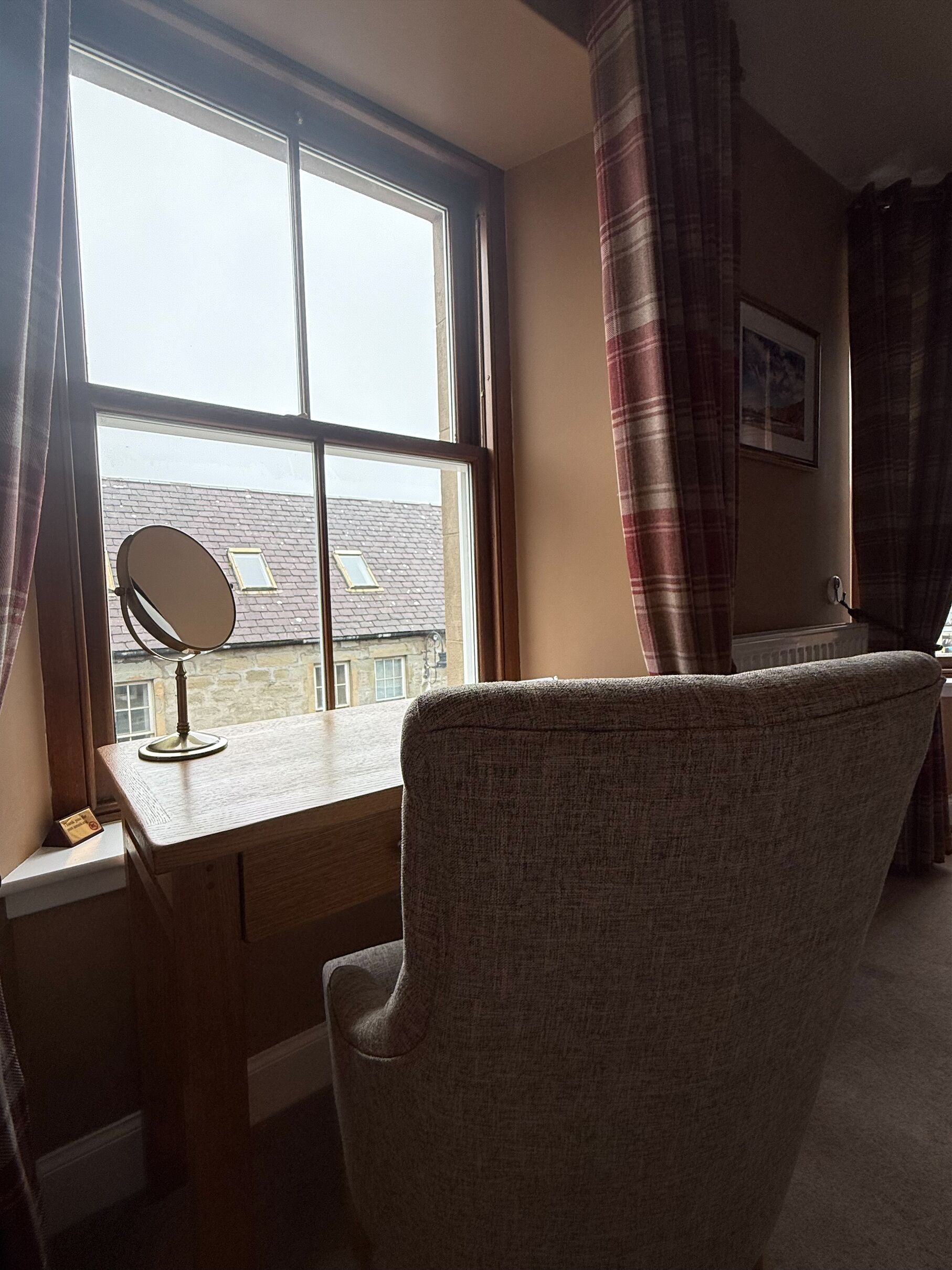 Une pièce comprenant un bureau, une chaise, une fenêtre avec des rideaux et un tableau accroché au mur.