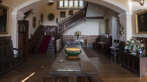 Un salón amplio con una mesa de madera, una escalera y retratos enmarcados en las paredes.