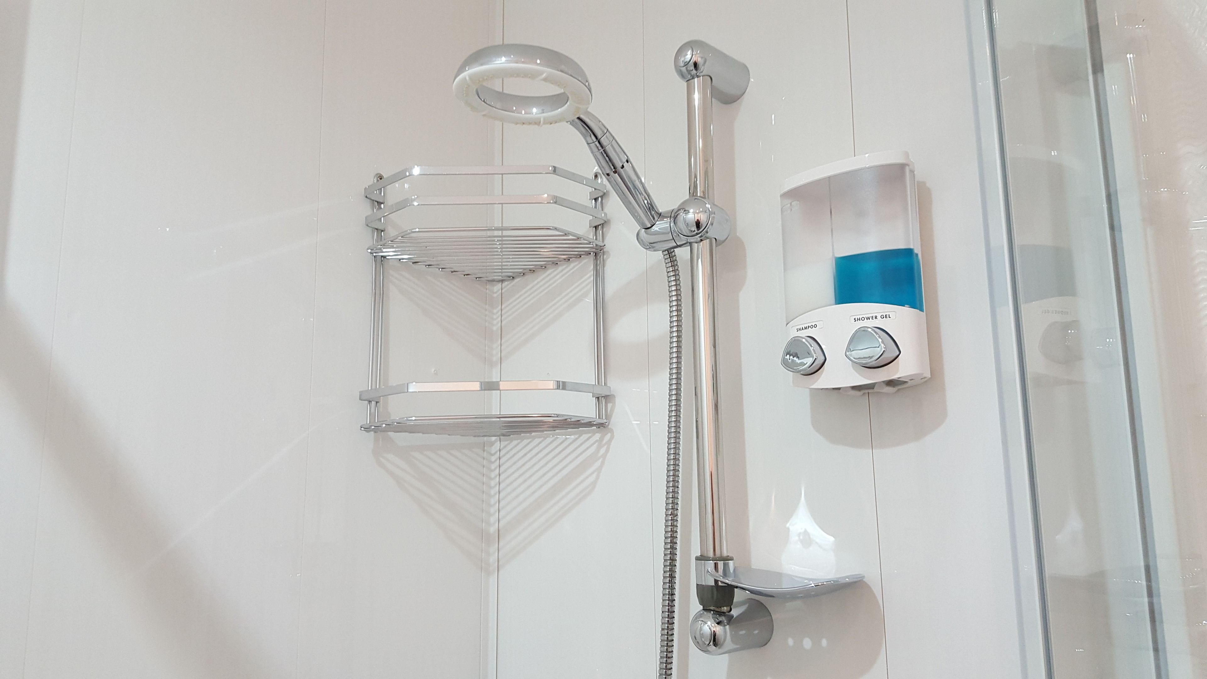 A shower with a chrome hose, a clear glass shelf, and a soap dispenser.