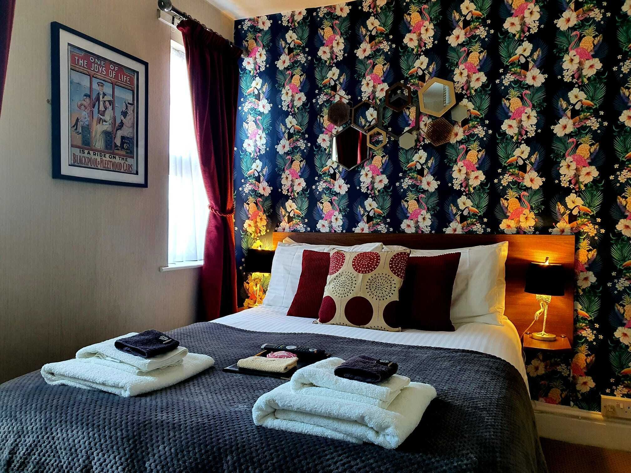 A hotel room with a bed, a framed picture on the wall, and a floral wallpaper.