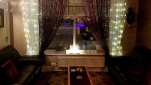 Un salon avec deux canapés en cuir, une table basse et une fenêtre agrémentée de rideaux et de guirlandes lumineuses.