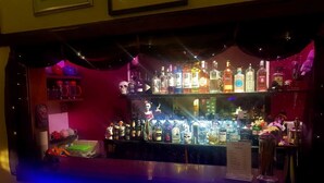 Un espace bar avec des étagères remplies de différentes bouteilles d’alcool, un présentoir pour les menus et des objets décoratifs.