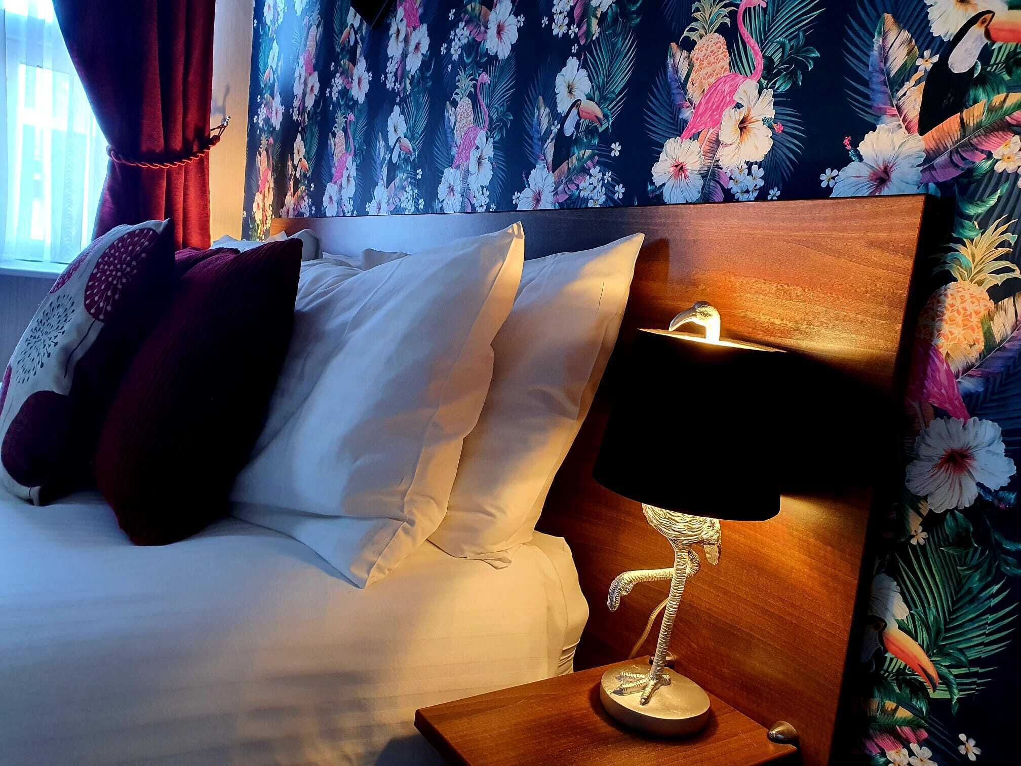 A hotel room with a bed, pillows, a nightstand, and a lamp.