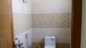 A small bathroom with a toilet, a shower, and a water heater mounted on the wall. - Hotel Krishna Grand Inn (Guntur)