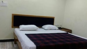 A single bed with a wooden headboard, white bedding, and a plaid blanket. - Hotel Krishna Grand Inn (Guntur)