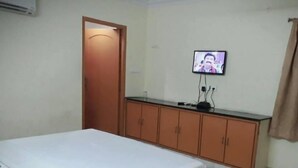 A bedroom with a bed, wooden wardrobe, and a television on the wall. - Hotel Krishna Grand Inn (Guntur)