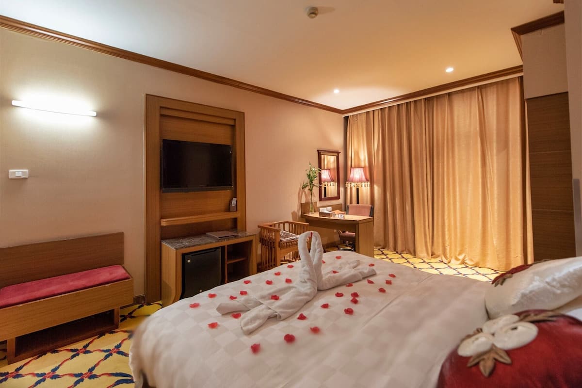 A hotel room with a bed, a TV, a desk, a chair, and a bedside table.