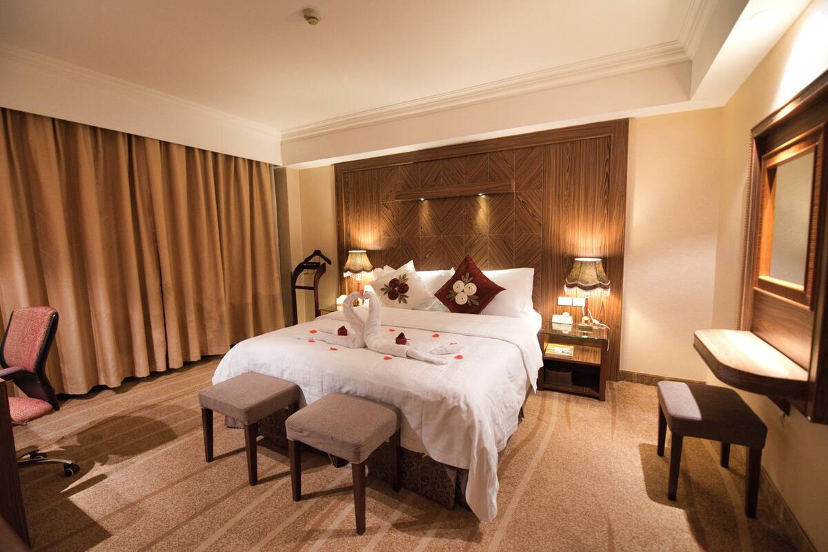 A hotel room with a large bed, two bedside tables, a chair, a bench, and a mirror.