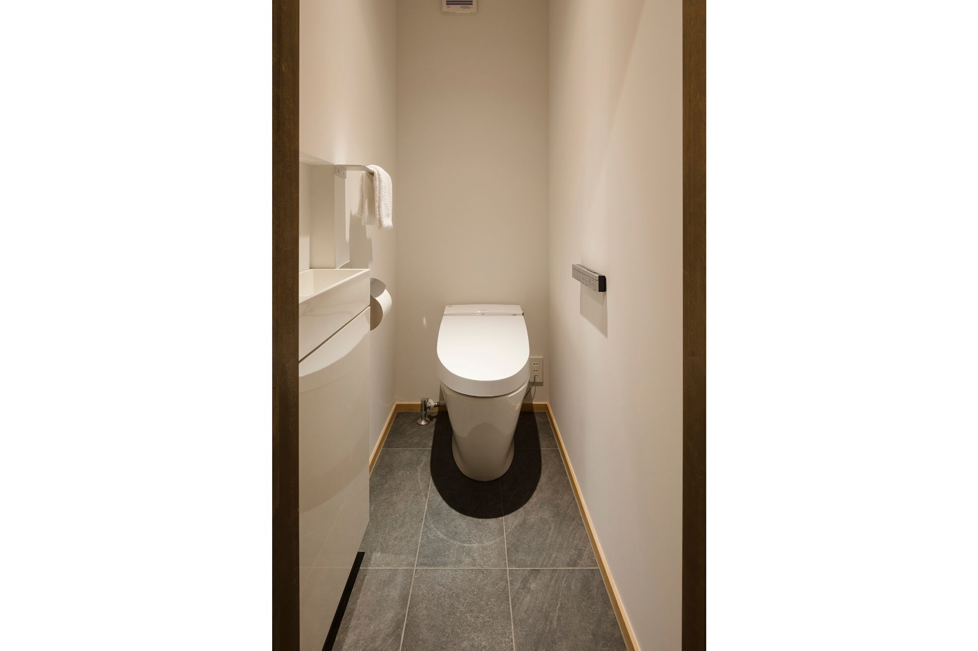 A narrow hallway with a toilet, a towel dispenser, and a small shelf.
