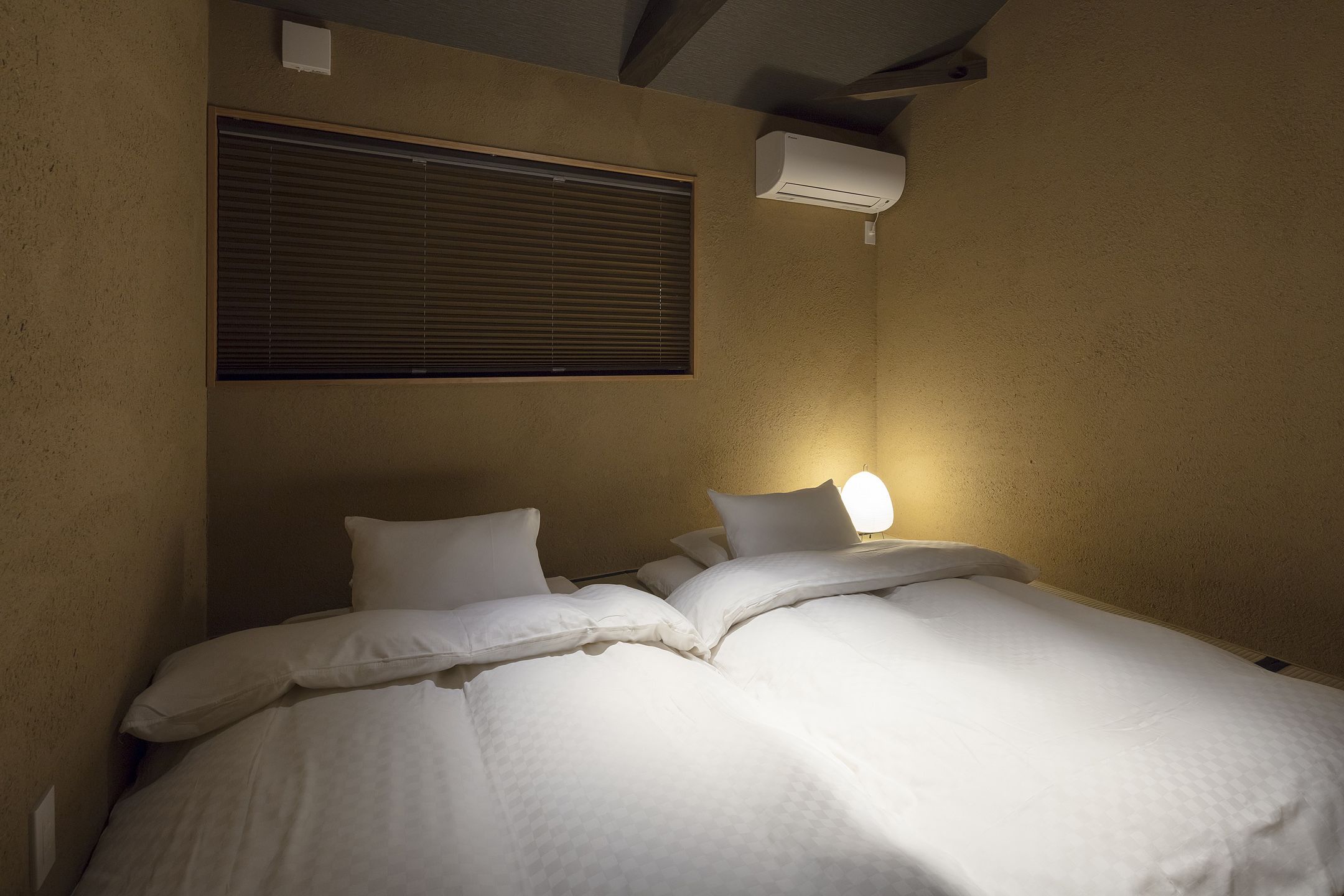A single bed with white bedding and a wall-mounted air conditioner above it.