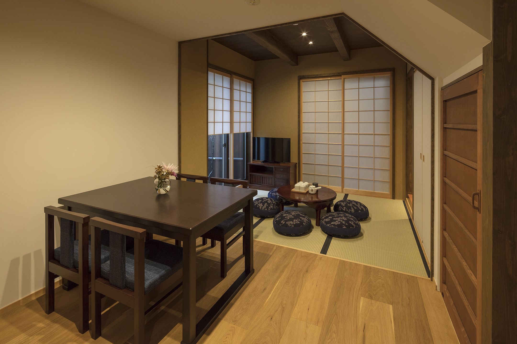 Ein traditioneller japanischer Raum mit Tatami-Böden, einem niedrigen Holztisch mit Kissen, einem Fernseher und Schiebetüren.