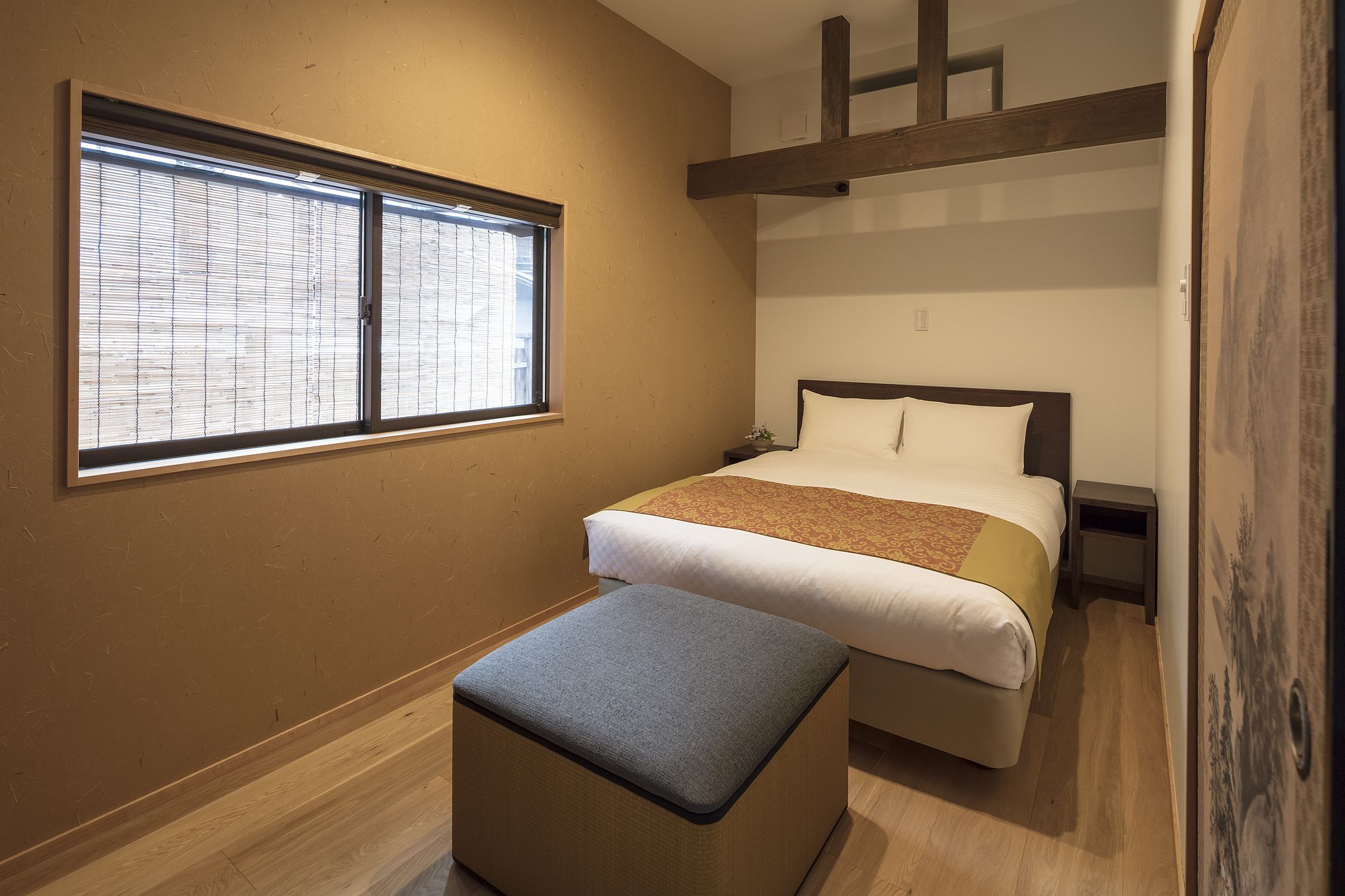 Un dormitorio con una cama, una ventana, un banco y estructura de vigas de madera.