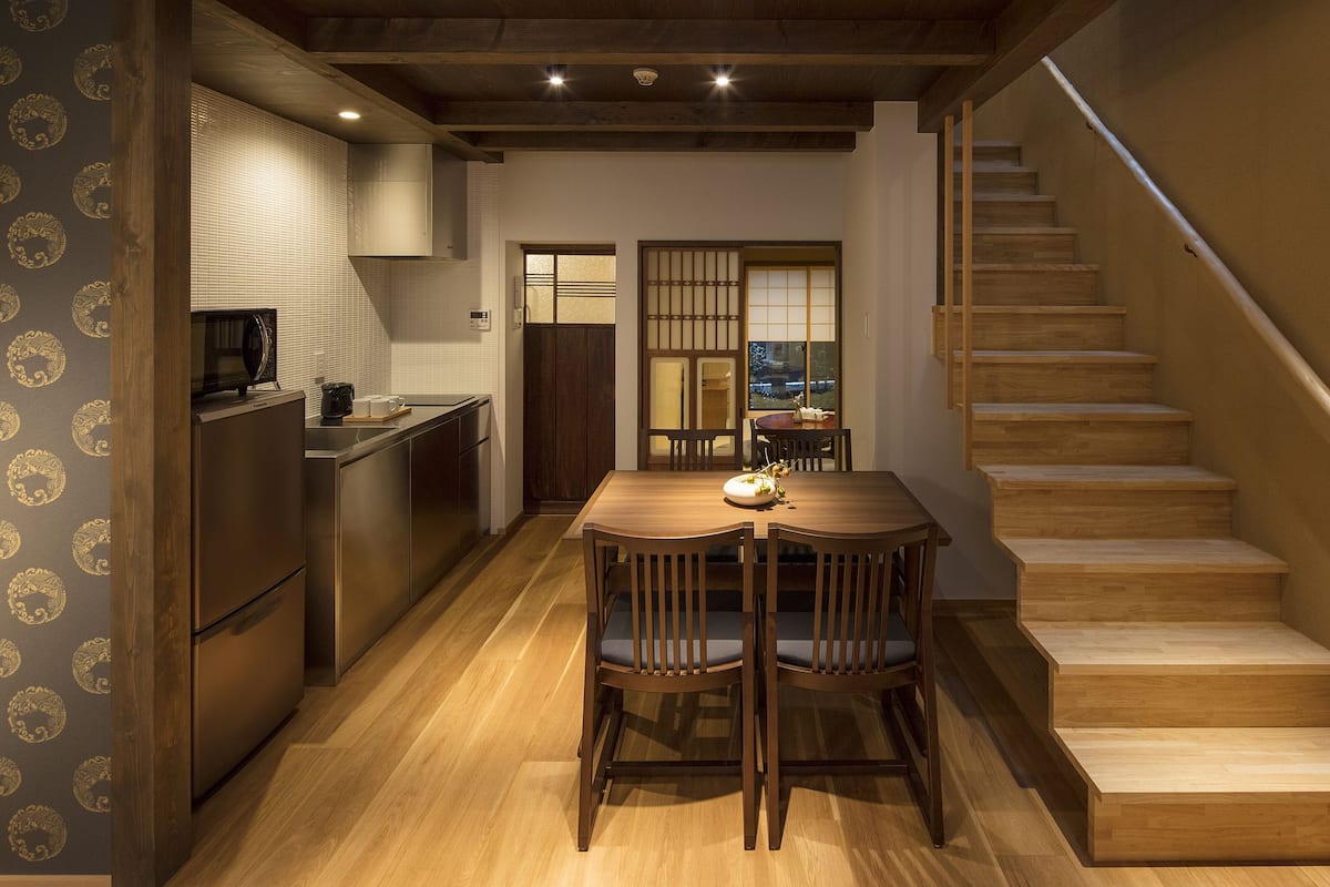 Une cuisine moderne avec une table et des chaises, un escalier en bois et une vue à travers un paravent japonais traditionnel.