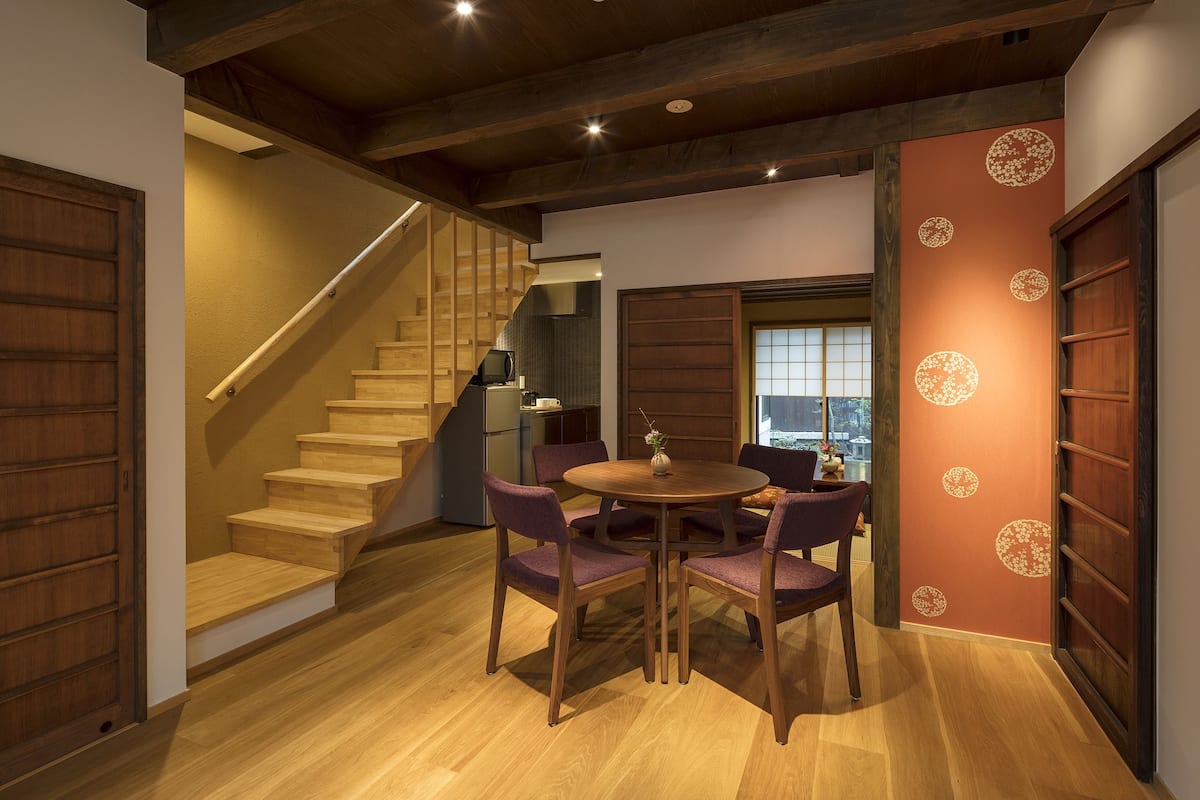 Un escalier en bois mène à un espace repas où se trouve une table ronde et des chaises violettes.