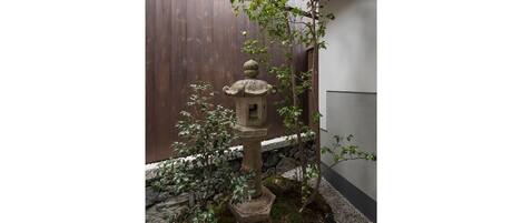 Un jardín japonés tradicional con un farol de piedra, un árbol pequeño y una valla de madera.