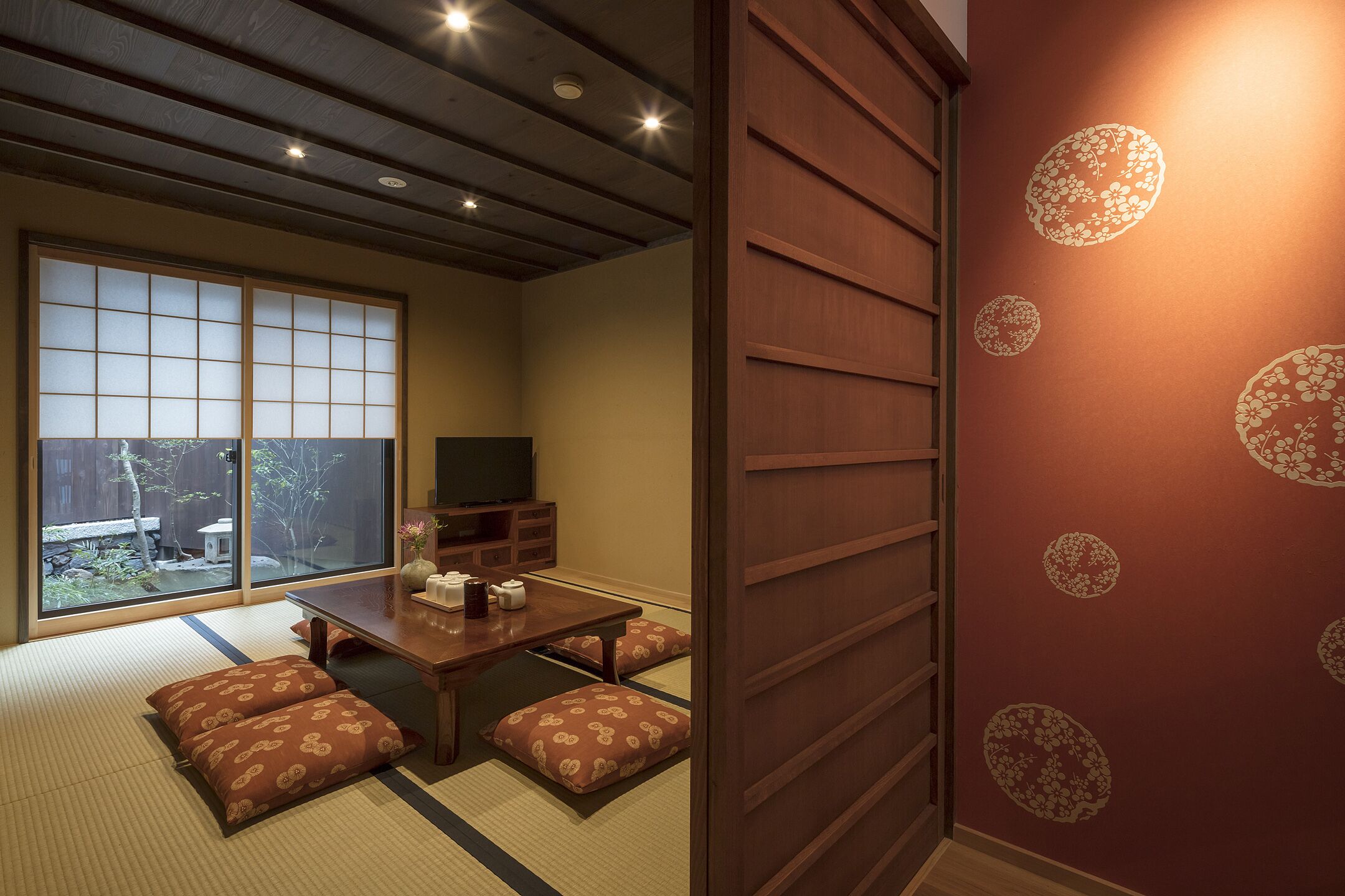 A traditional Japanese room with tatami flooring, a low table with cushions, a television, and sliding doors.